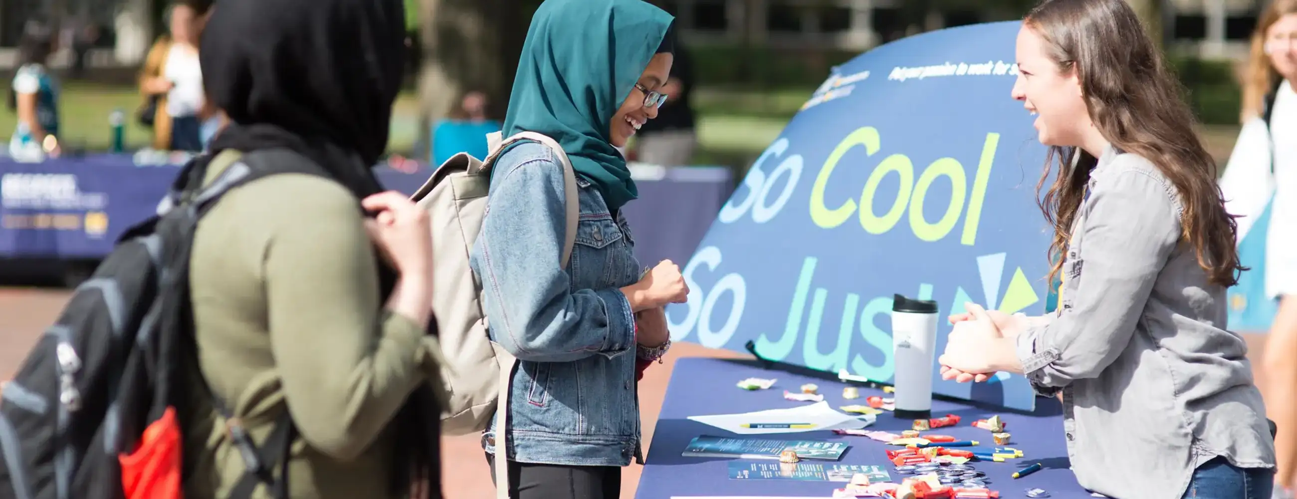 Students at the So Cool So Just fair on the Diag speaking at a table outside.