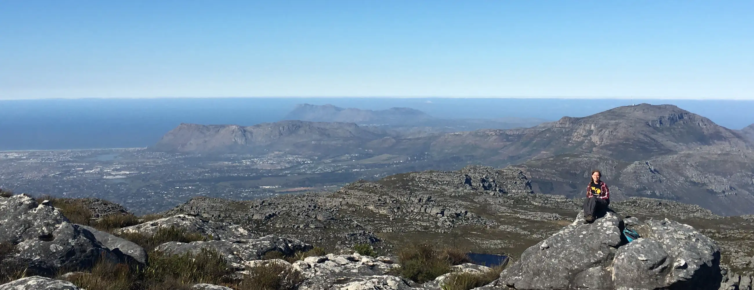 A mountain range leading into an ocean with a student sitting in the bottom left of the image.