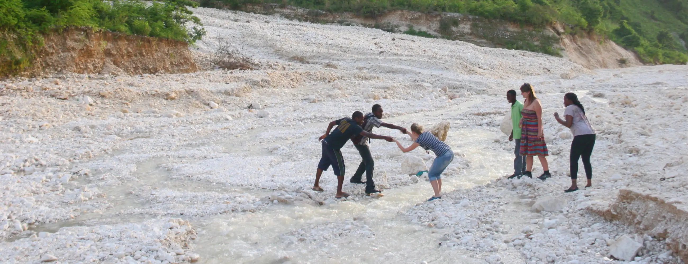 Two people helping another across a small river