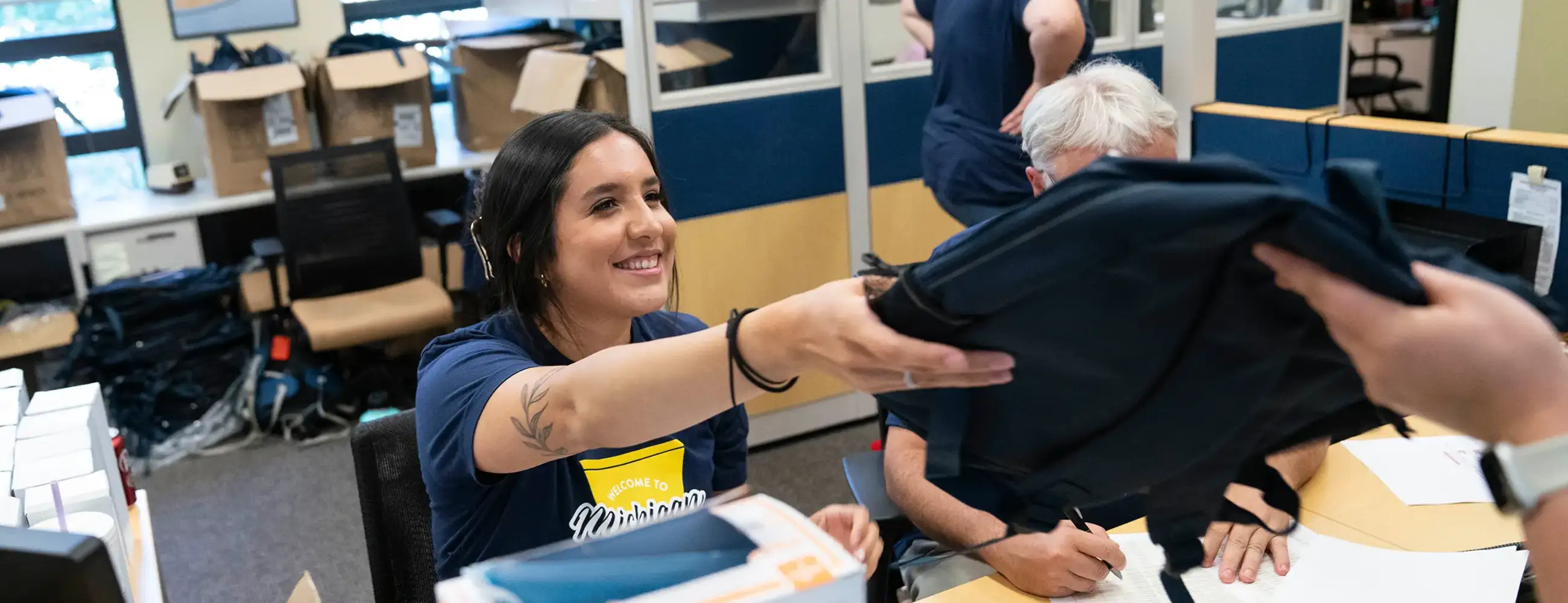 A work-study student handing out backpacks to newly admitted students during orientation.