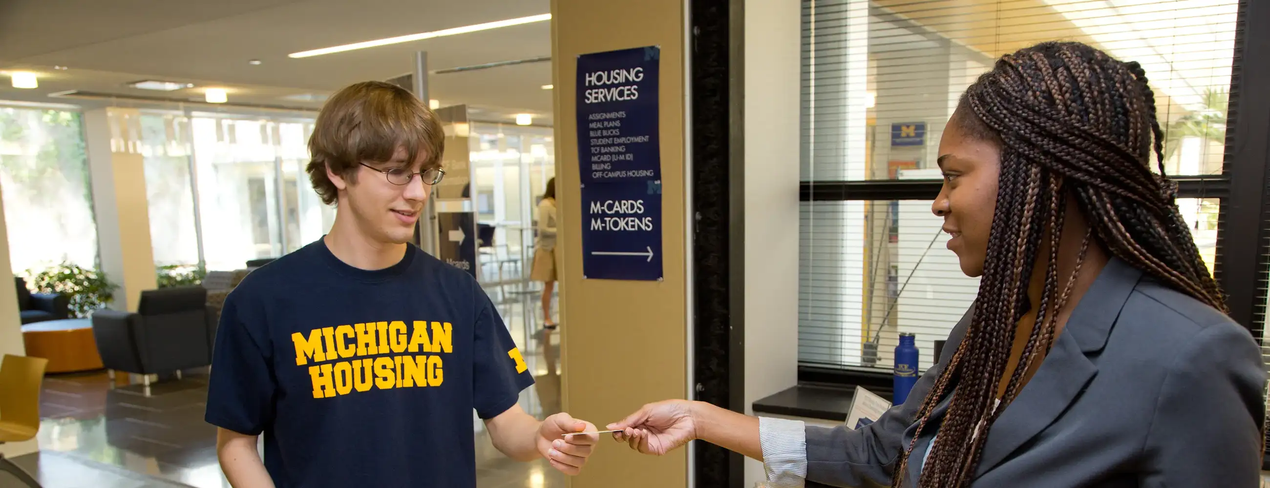 One student standing at a counter with another person handing them an MCard.