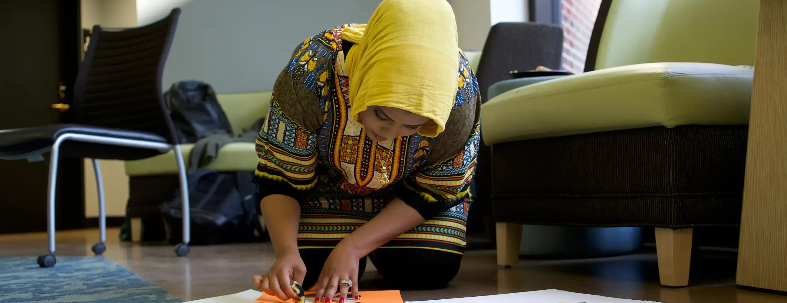 Photo of a student wearing a hijab kneeling and working on a poster.