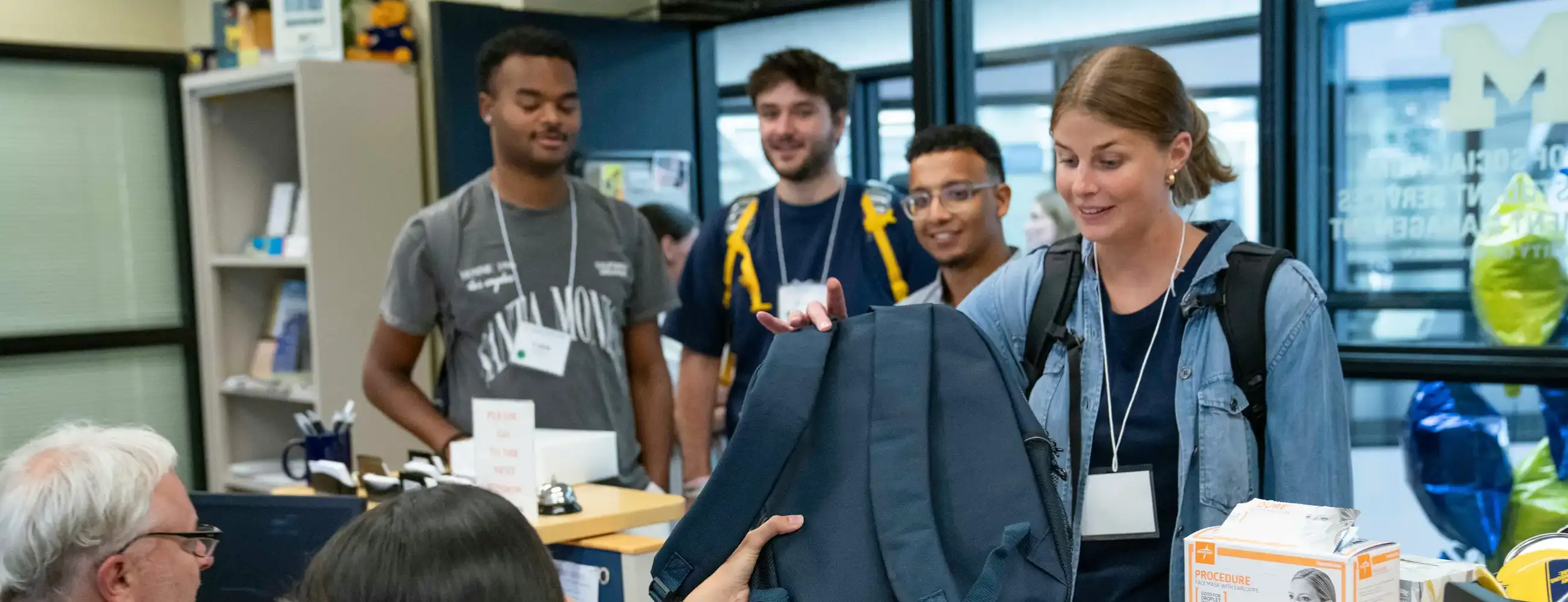 Students receive a backpack at a campus check-in table with staff and supplies visible.