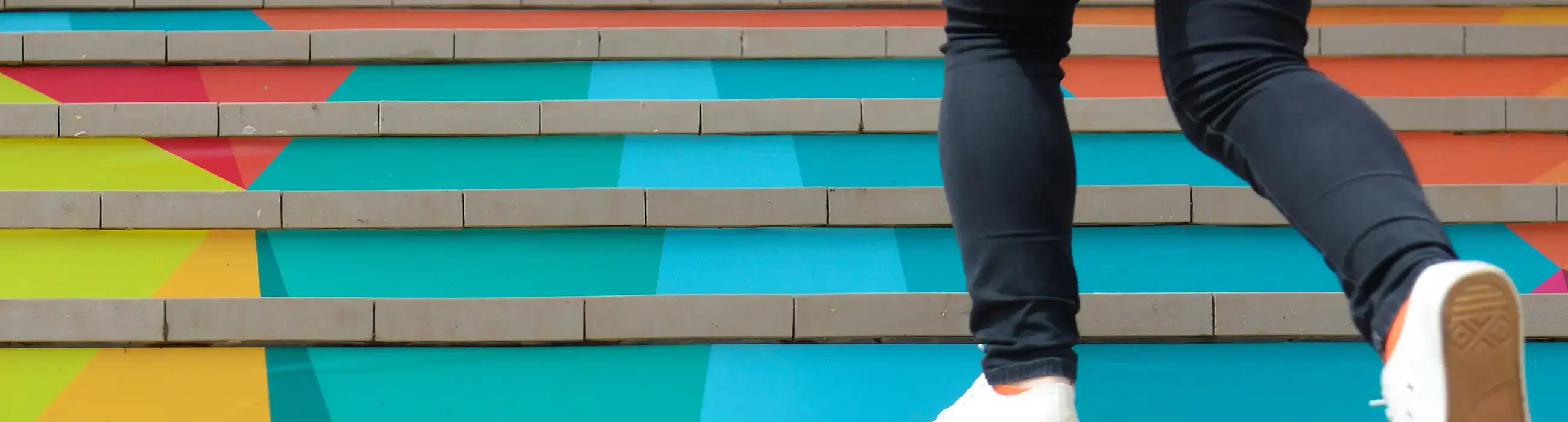 Image of a person walking up colorful stairs. You can only see the person's feet.