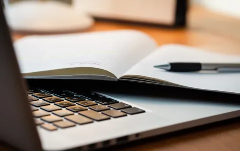 A computer and pad of paper with a pen laying on top