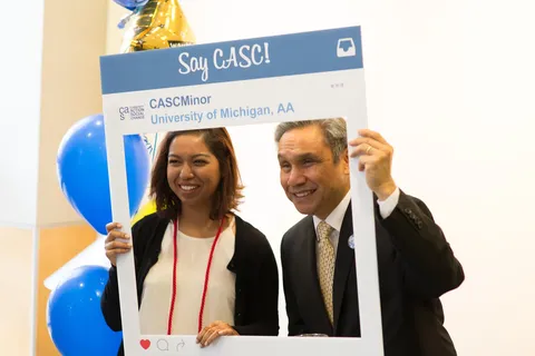 An instructor and student standing in front of balloons smiling with a poster that says "Say CASC!"