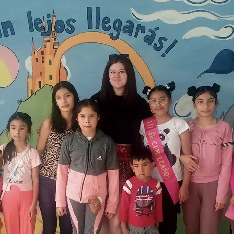 Photo of Jordan Lummus with six children in front of a blue mural
