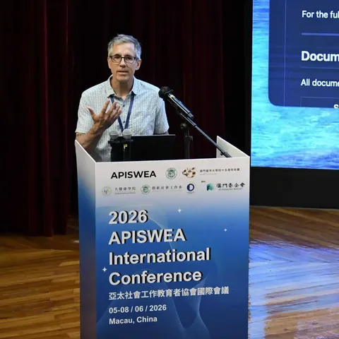 alt text. this is Brian PerronFormulated accessible alt text for speaker photographFormulated accessible alt text for speaker photographBrian Perron speaks at a podium during the 2026 APISWEA International Conference in Macau, China. He gestures with one hand while addressing the audience. The podium displays the conference banner reading "2026 APISWEA International Conference" with the dates 05-08/06/2026, and a presentation slide is projected on a screen behind him.
