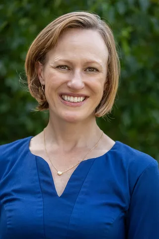 Headshot of Jamie Oberlander wearing a blue top in front of foliage.