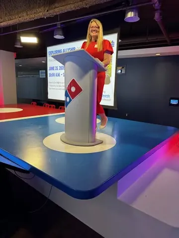 Katie Edwards smiles behind a Domino's-branded podium while giving a Pride Month keynote at Domino's global headquarters.
